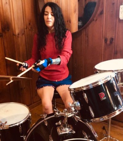 Bernadette playing the drums with the drumsticks held in the small item gripping aids. The palm pads allow you to angle the drumsticks exactly how you want them