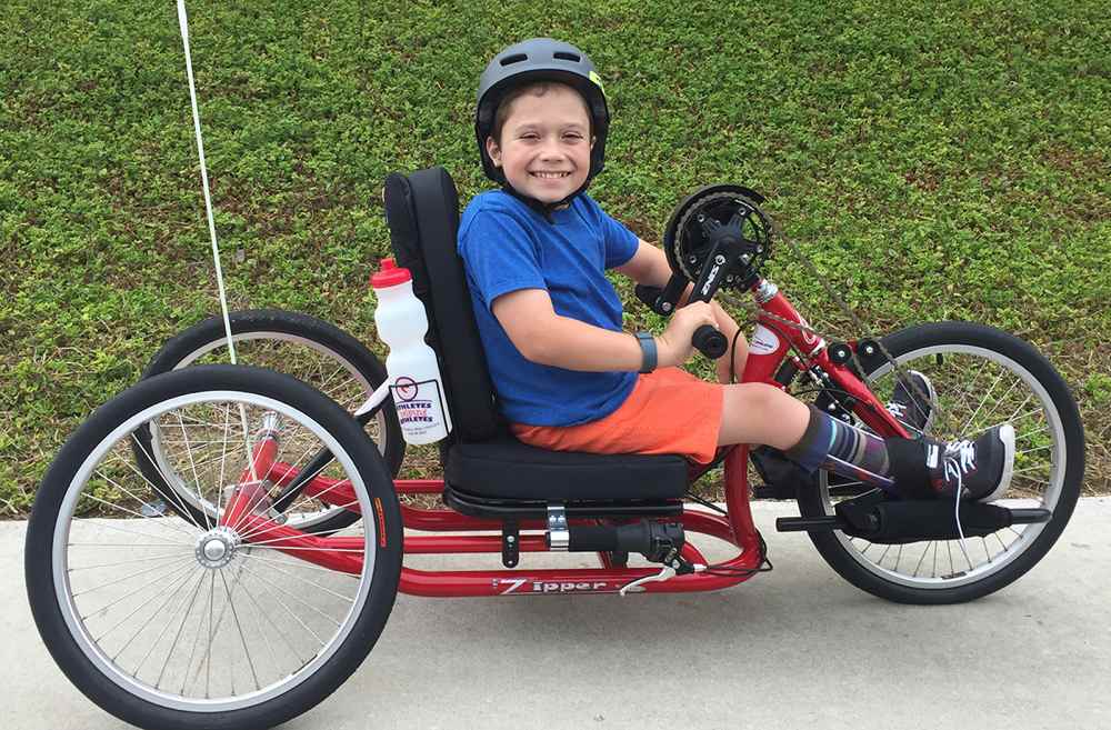A smiling boy rides his hand bike