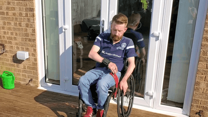 Gareth uses therabands to do a diagonal row using his wheelchair to hold one end of the band and a hook aid to hold the other