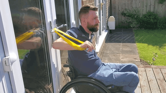 a gif of Gareth doing a one-armed chest press with a yellow theraband while sat outside