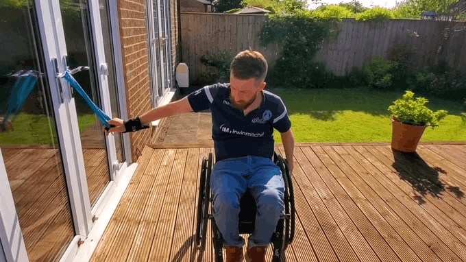 a gift showing Gareth doing exercise with a theraband outside in the sunshine. He is using a hook aid to hold the band