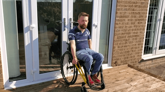 Gareth uses a yellow theraband to exercise on his deck in the sunshine