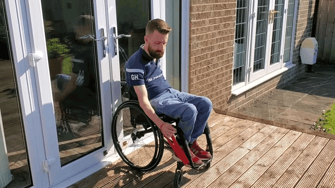 a gif of Gareth doing a bicep curl with a red theraband sat in his wheelchair outside in the sunshine